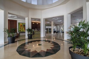 Un hall amplio con un piso de diseño geométrico central, varias zonas de estar y plantas en macetas.