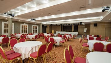 Un salón de banquetes con mesas redondas y sillas rojas, equipado con proyectores y luces instalados en el techo.