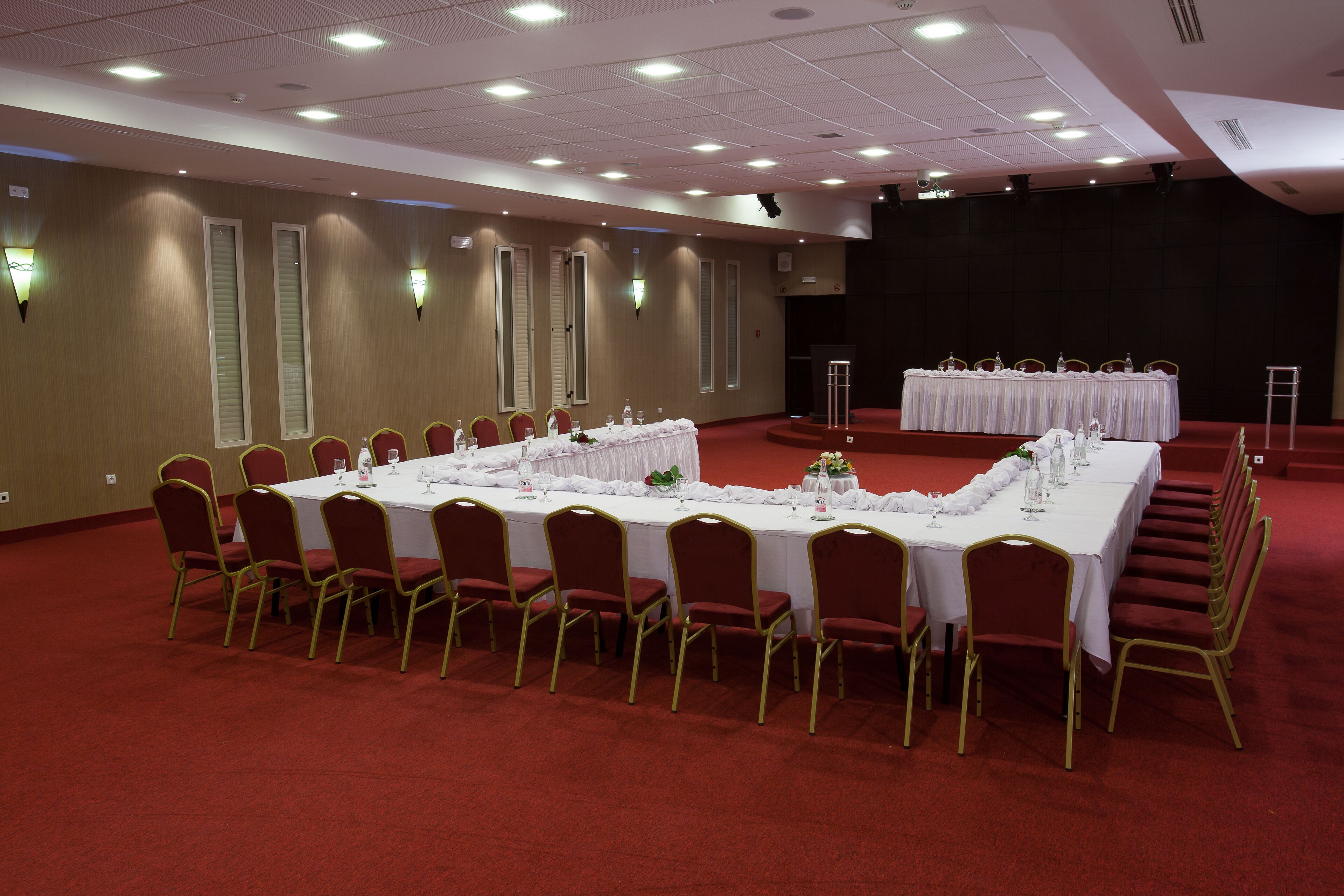 Une salle de conférence avec une longue table préparée pour une réunion, entourée de chaises, et un espace dédié à la présentation avec un pupitre.