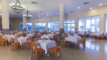 Un comedor amplio con varias mesas y sillas, ventanas grandes y candelabros.