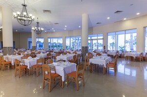 Un comedor amplio con varias mesas y sillas, ventanas grandes y candelabros.