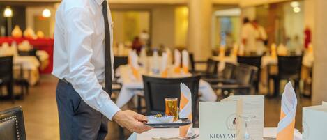 A waiter serving a dish at a restaurant table with a menu and a wine glass.
