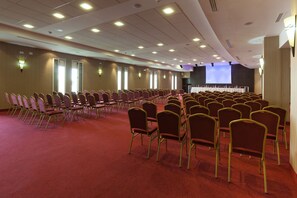A conference room with rows of chairs, a stage with a projector screen, and a carpeted floor. - Khayam Garden Beach Resort & Spa (Nabeul)