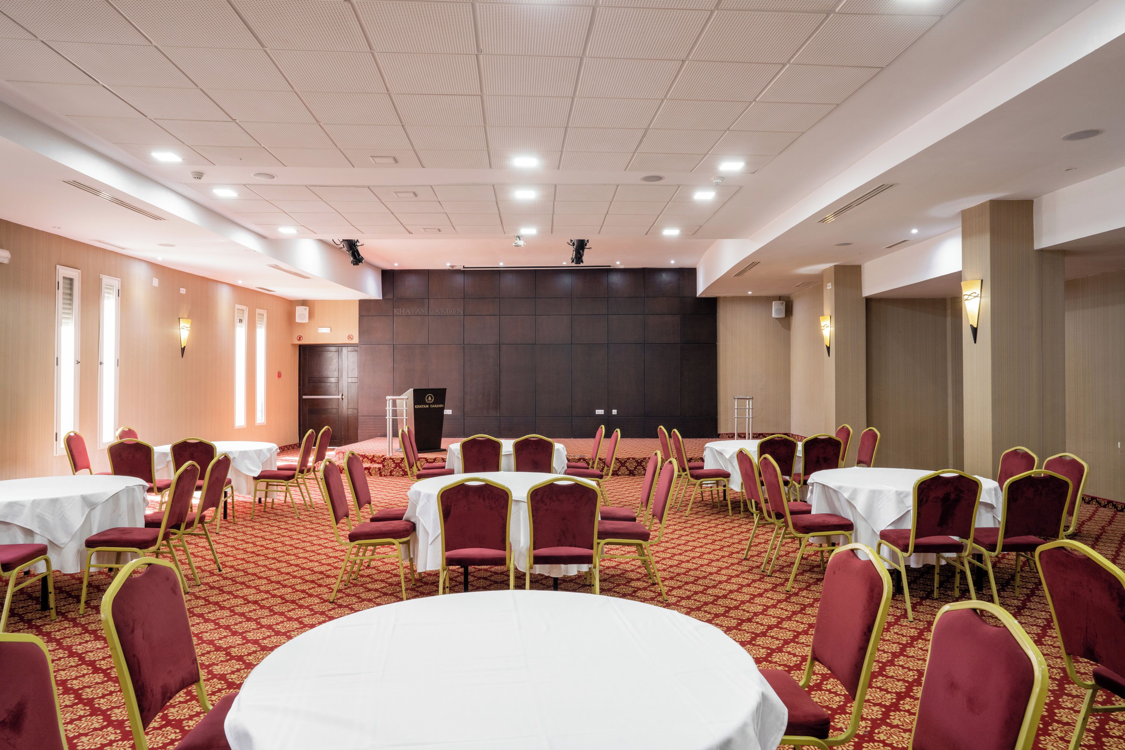 A conference room with multiple tables and chairs, a stage, and a podium.