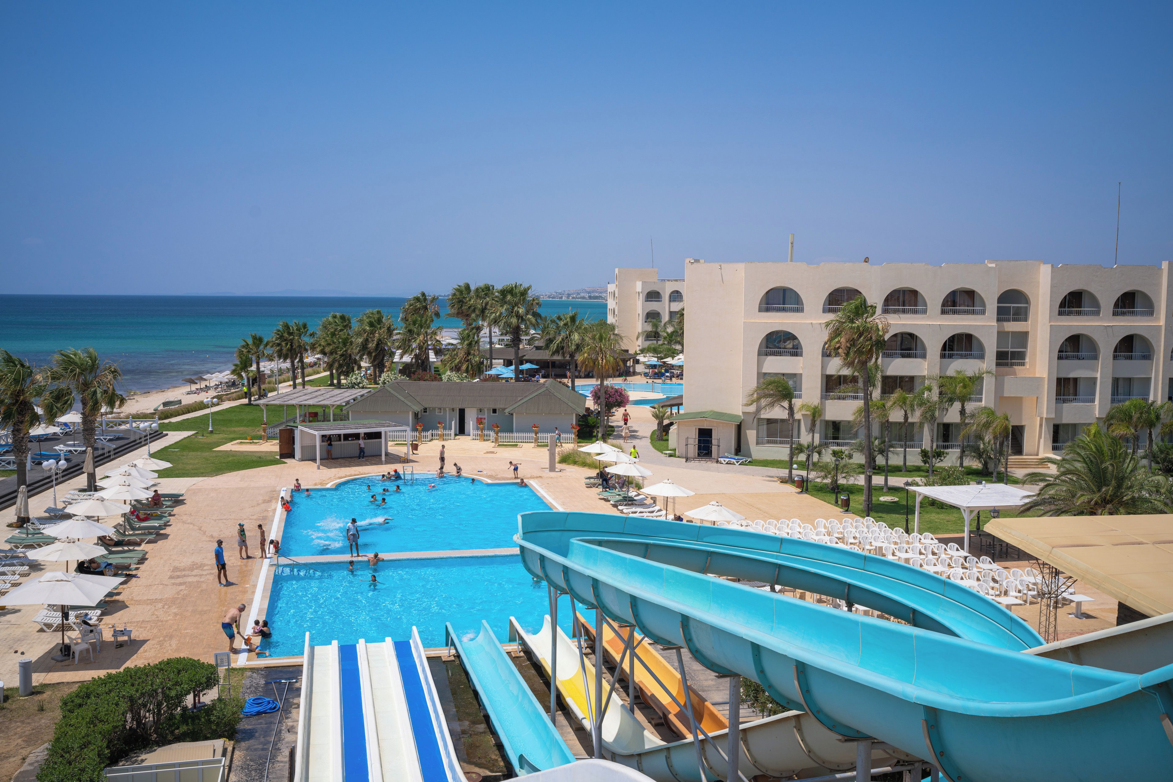 Un resort con piscina, toboganes acuáticos, sillas de playa y vista al océano.