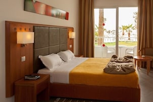 Habitación de hotel con una cama grande, dos lámparas de noche, cabecera de madera y vistas al exterior a través de una puerta corrediza de vidrio.