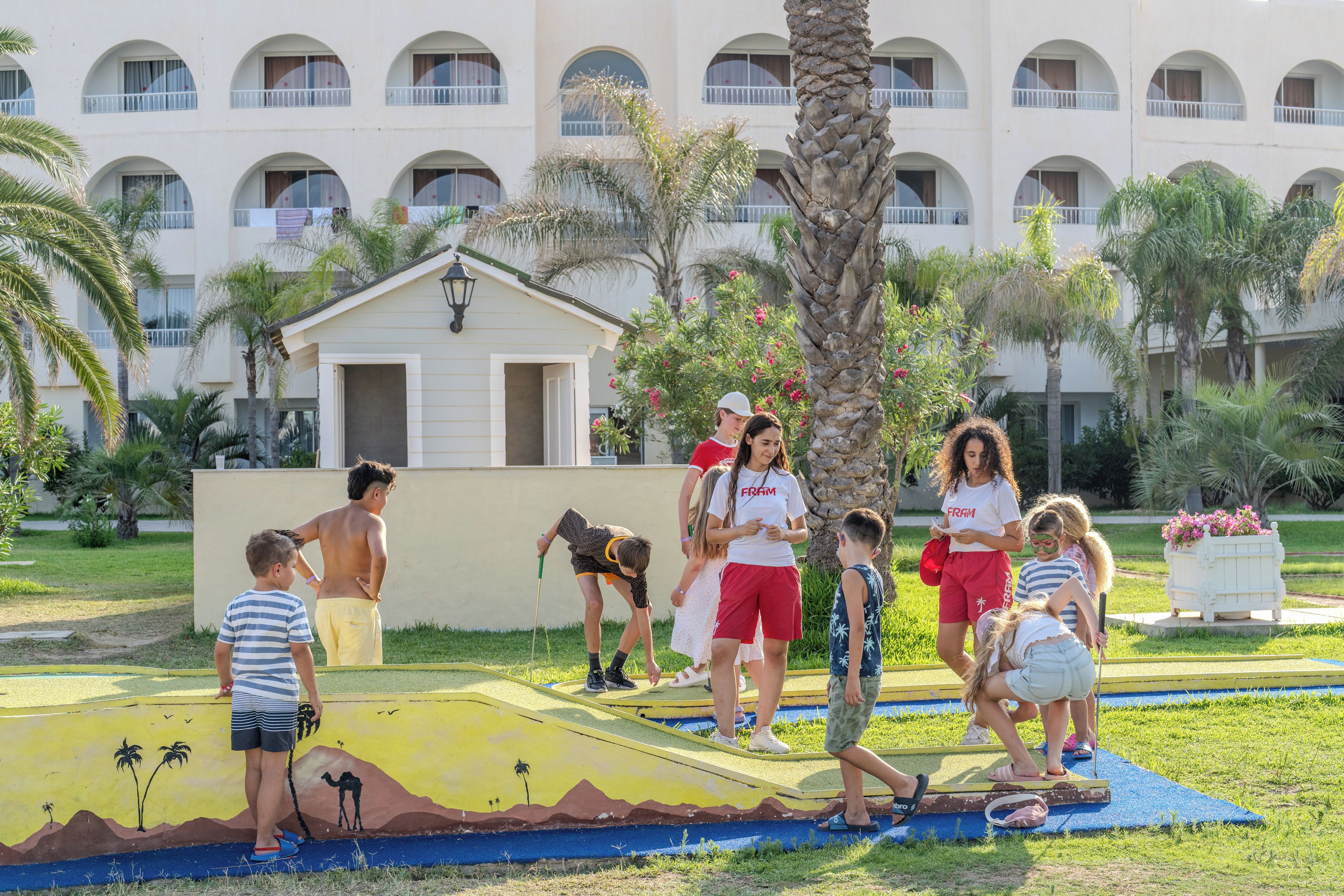 A group of people playing on a colorful outdoor play area with palm trees and a building in the background.