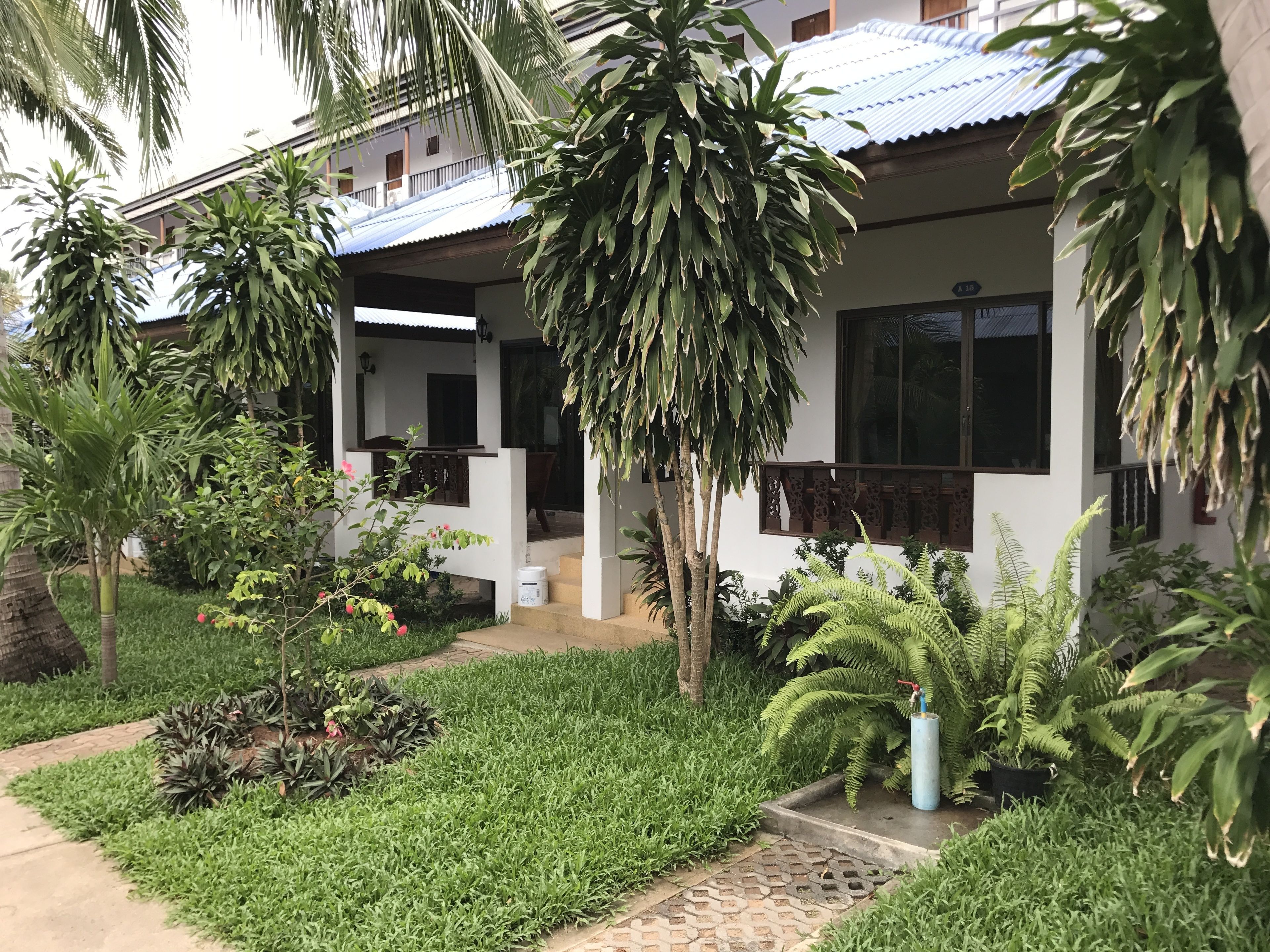 A modern building with a covered outdoor area, surrounded by lush greenery and palm trees.