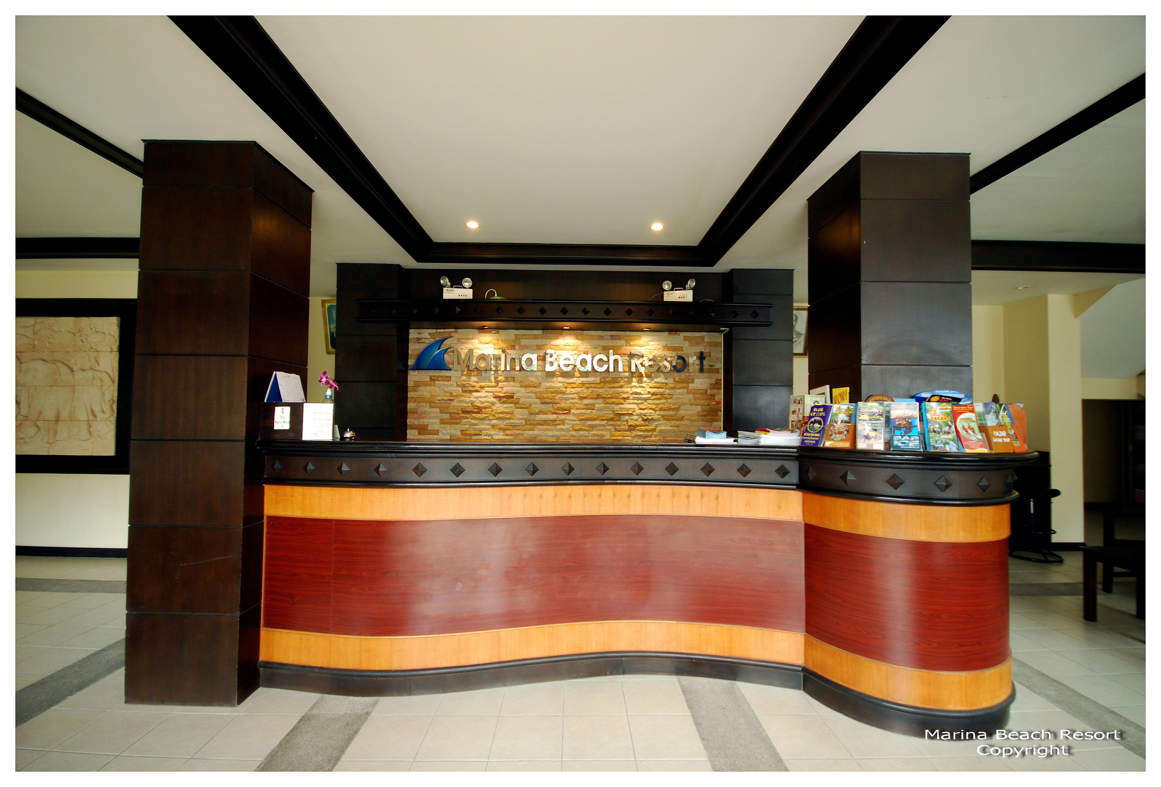 A reception desk at Marina Beach Resort with a stone wall backdrop, a wooden counter, and a display of brochures.