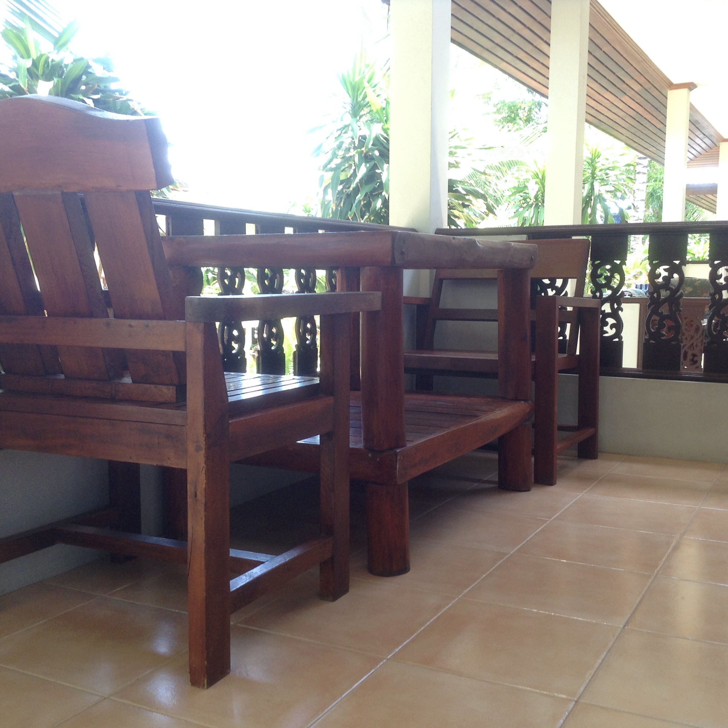A row of wooden chairs with a tiled floor and a railing with decorative elements.