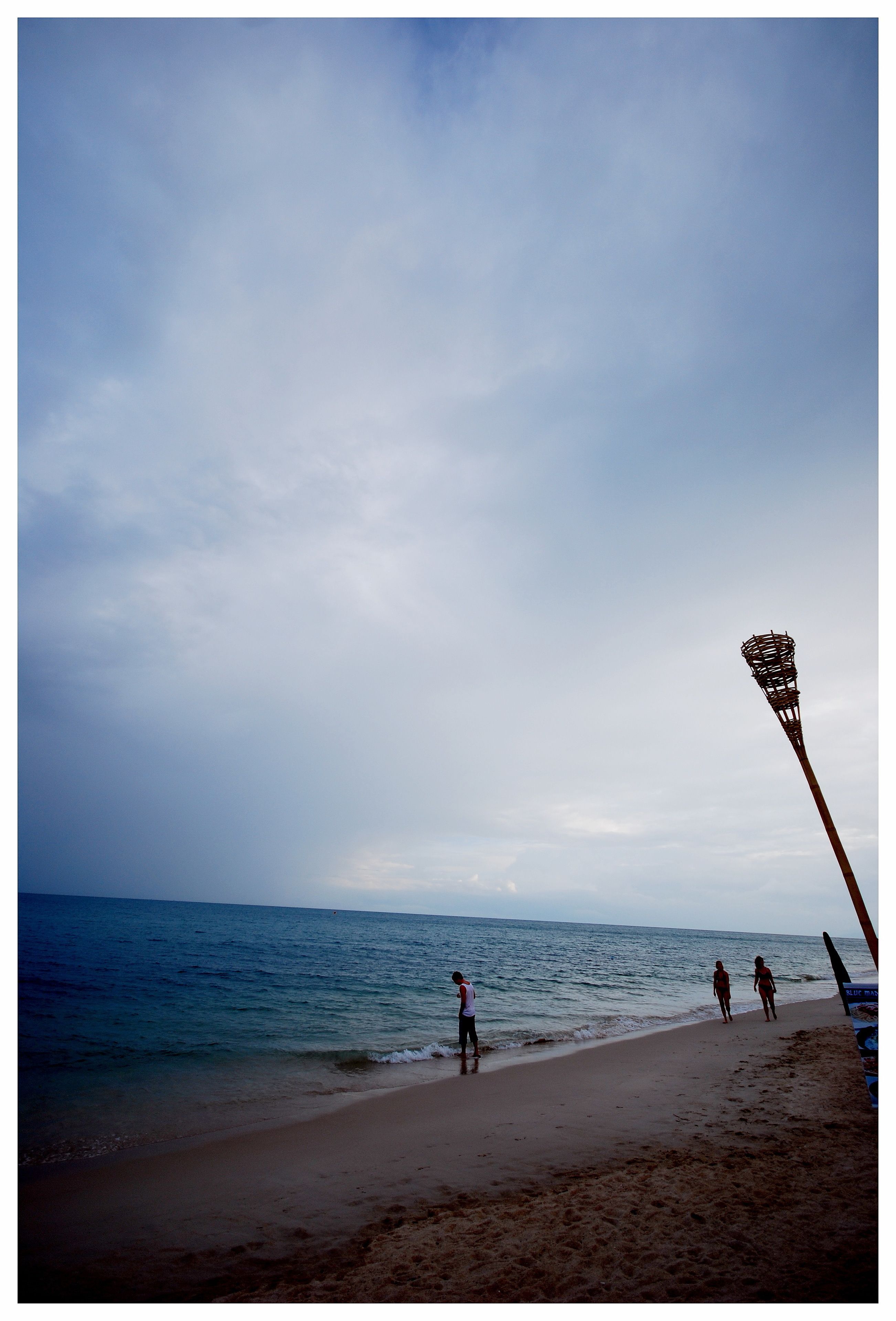 Een strand met een lacrosse doelpaal en mensen die langs de kust wandelen.