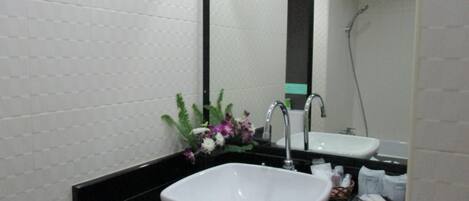 Un baño con lavabo blanco, encimera negra y un espejo que refleja la zona de la ducha.