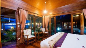 A wooden room with a bed, two chairs, and a table. There are curtains and a view of the outside. - Lipa Bay Resort (Koh Samui)