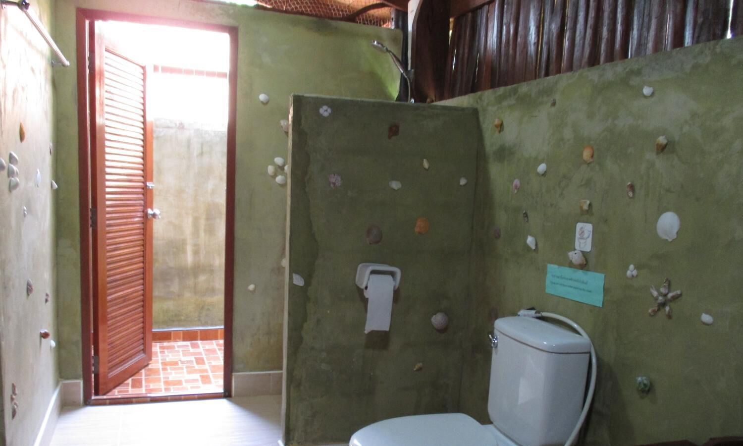 A bathroom with a toilet, a towel dispenser, and a door leading to an outdoor area.