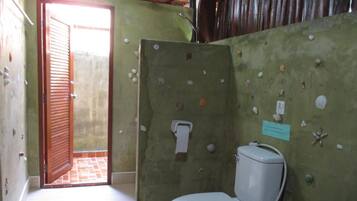 A bathroom with a toilet, a towel dispenser, and a door leading to an outdoor area.