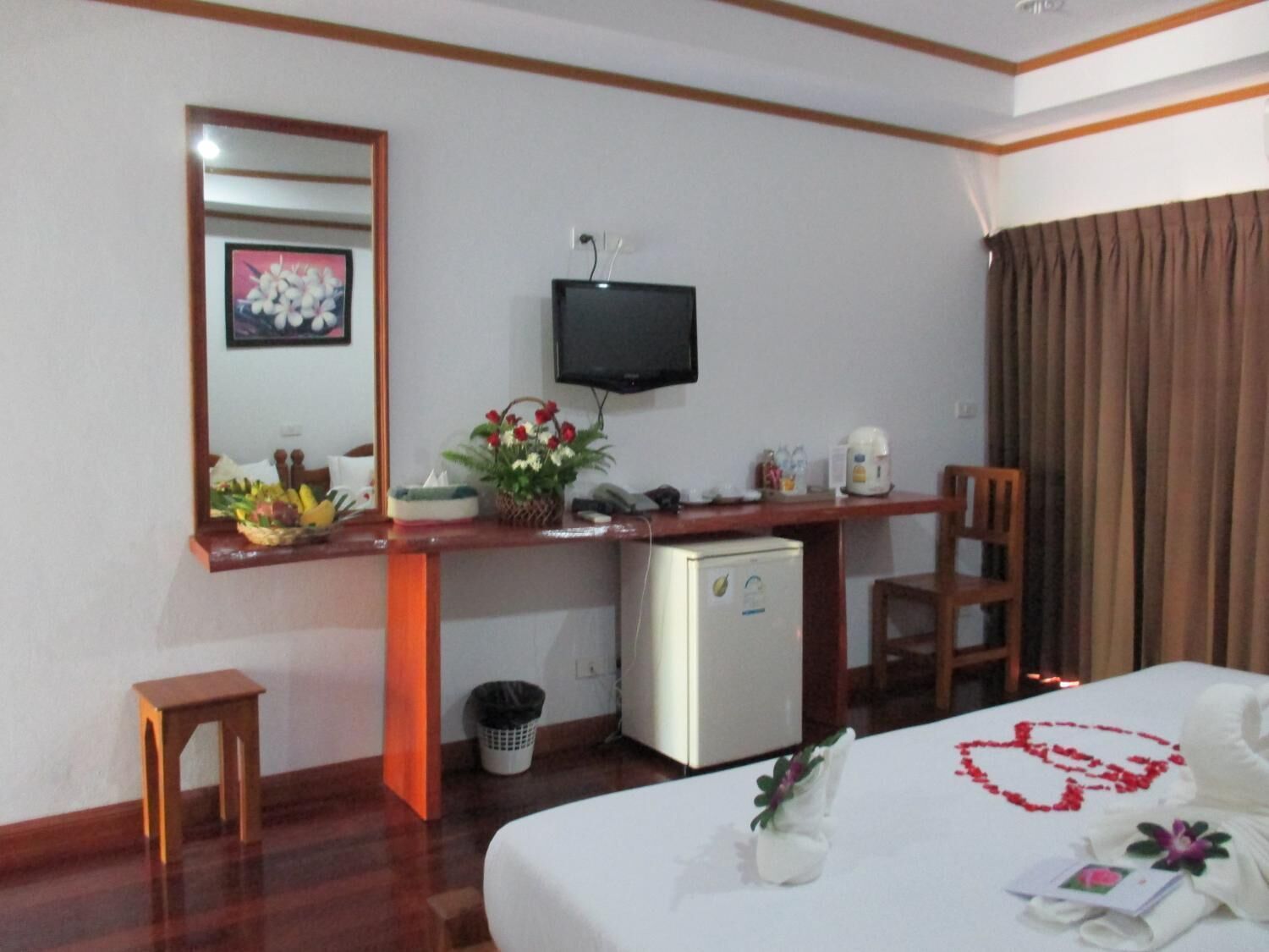 A hotel room with a bed, a desk with a television, a small refrigerator, and a trash bin.