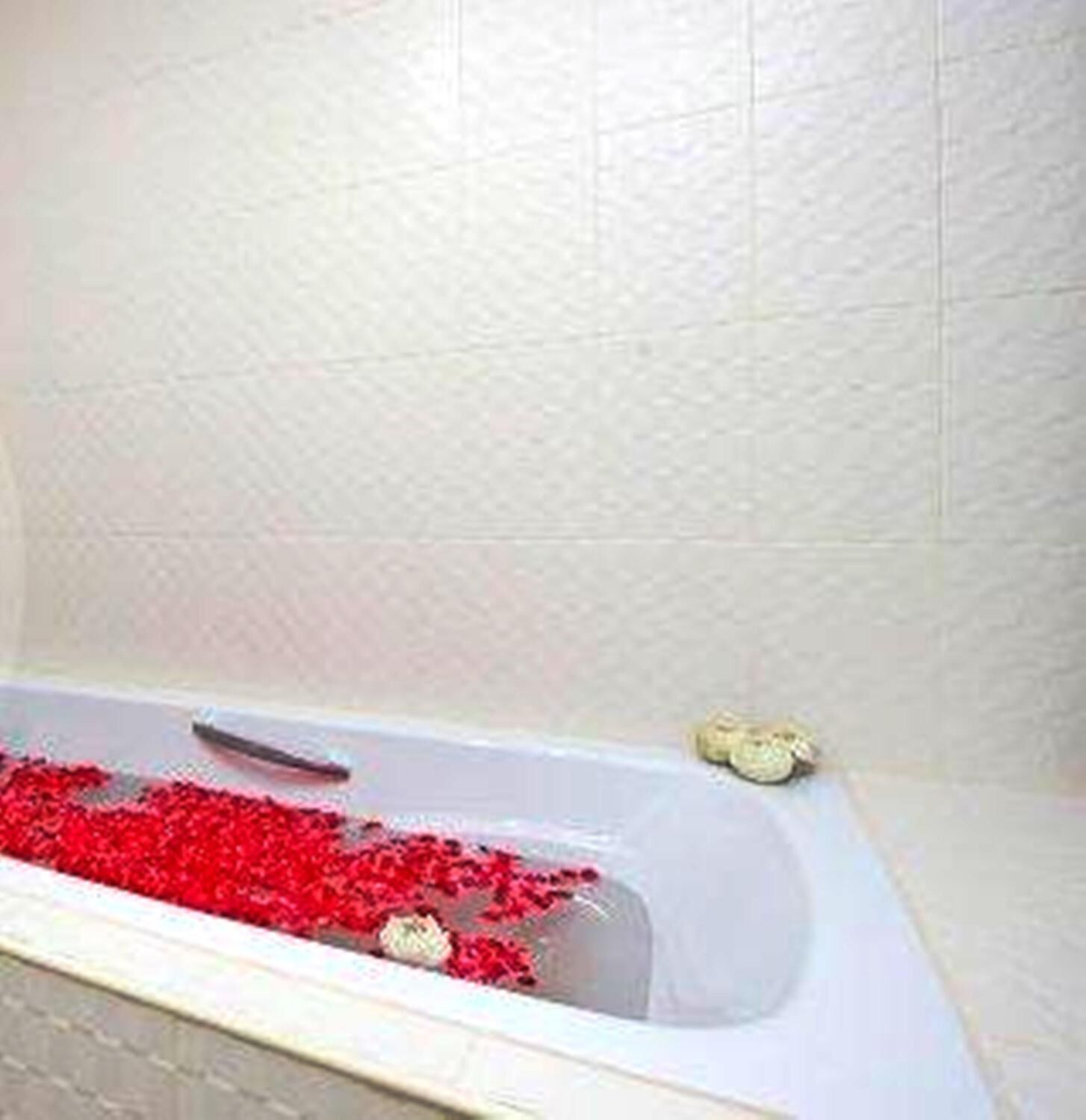 Una bañera llena de productos de baño rojos y una alfombra blanca para baño.