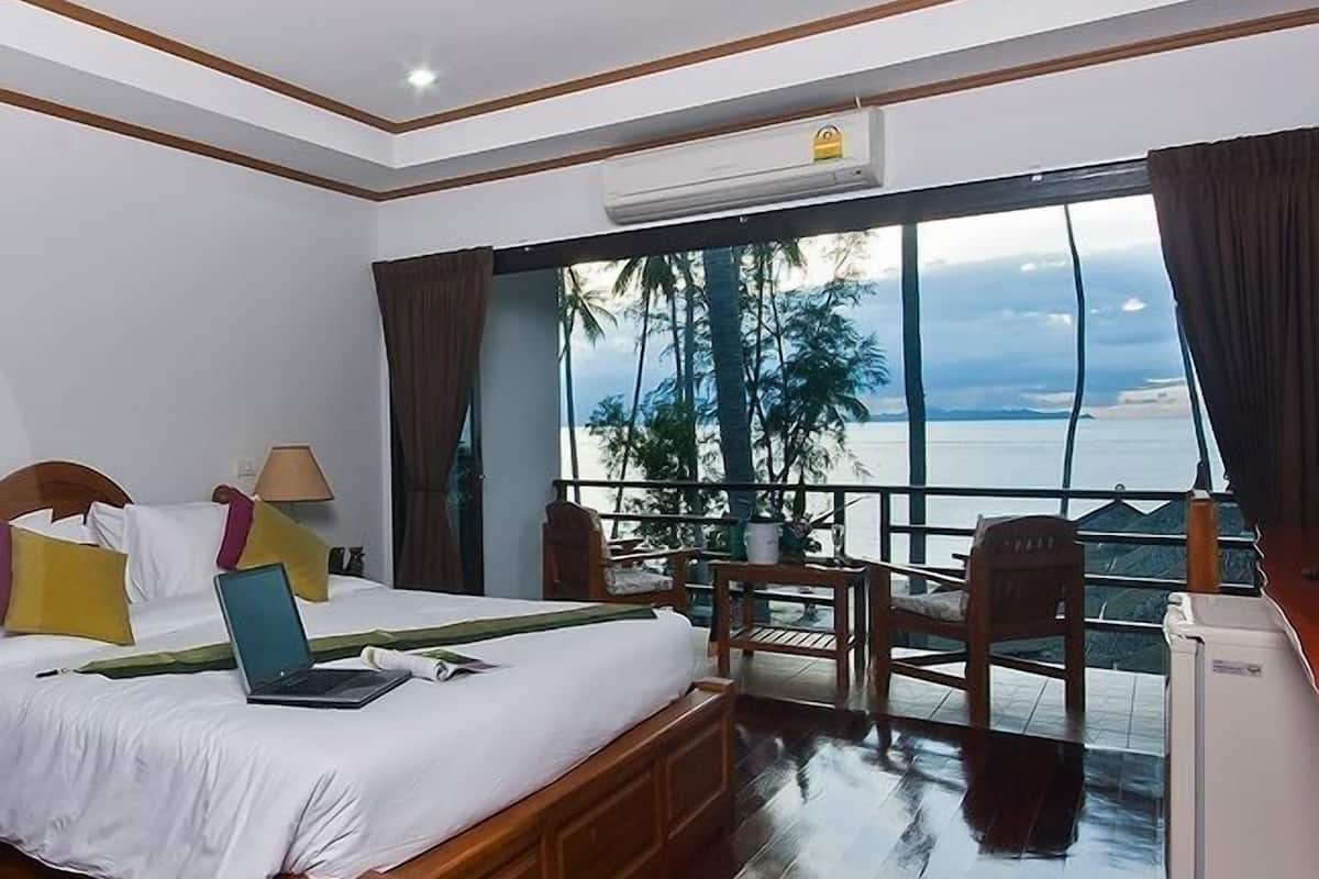 A hotel room with a bed, a desk, a chair, and a view of the sea.