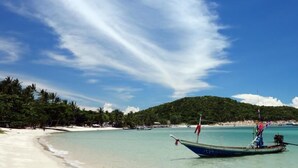 A beach with a boat, clear turquoise water, and a hill in the background. - Lipa Bay Resort (Koh Samui)