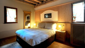 Un dormitorio con techo de madera, una cama con colcha blanca, dos lámparas de noche y un ventanal con cortina.