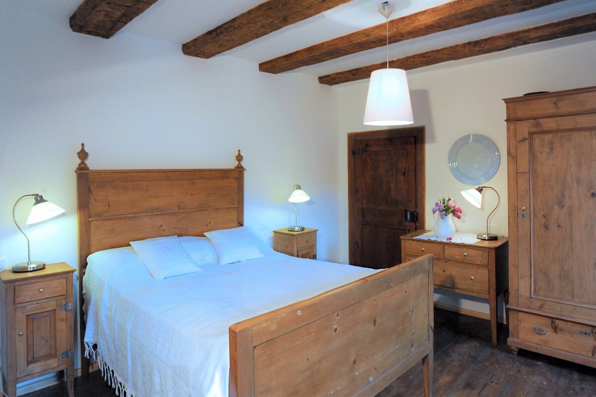 A bedroom with a wooden bed, bedside tables with lamps, a wooden wardrobe, and a wooden ceiling with exposed beams.