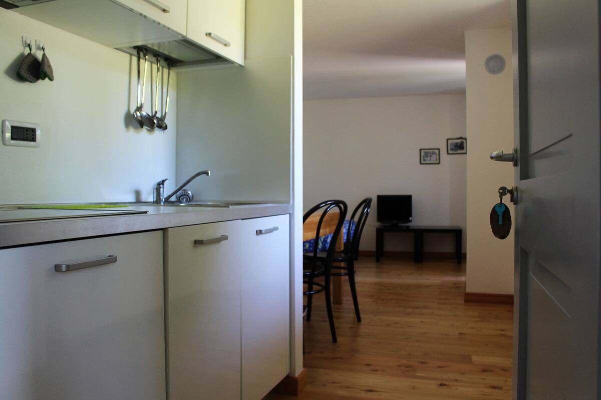 A kitchen with white cabinets, a sink, and hanging utensils. There is a dining area with a table and chairs.