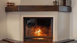 Una chimenea con fuego, un repisa de madera y una cesta de leña.