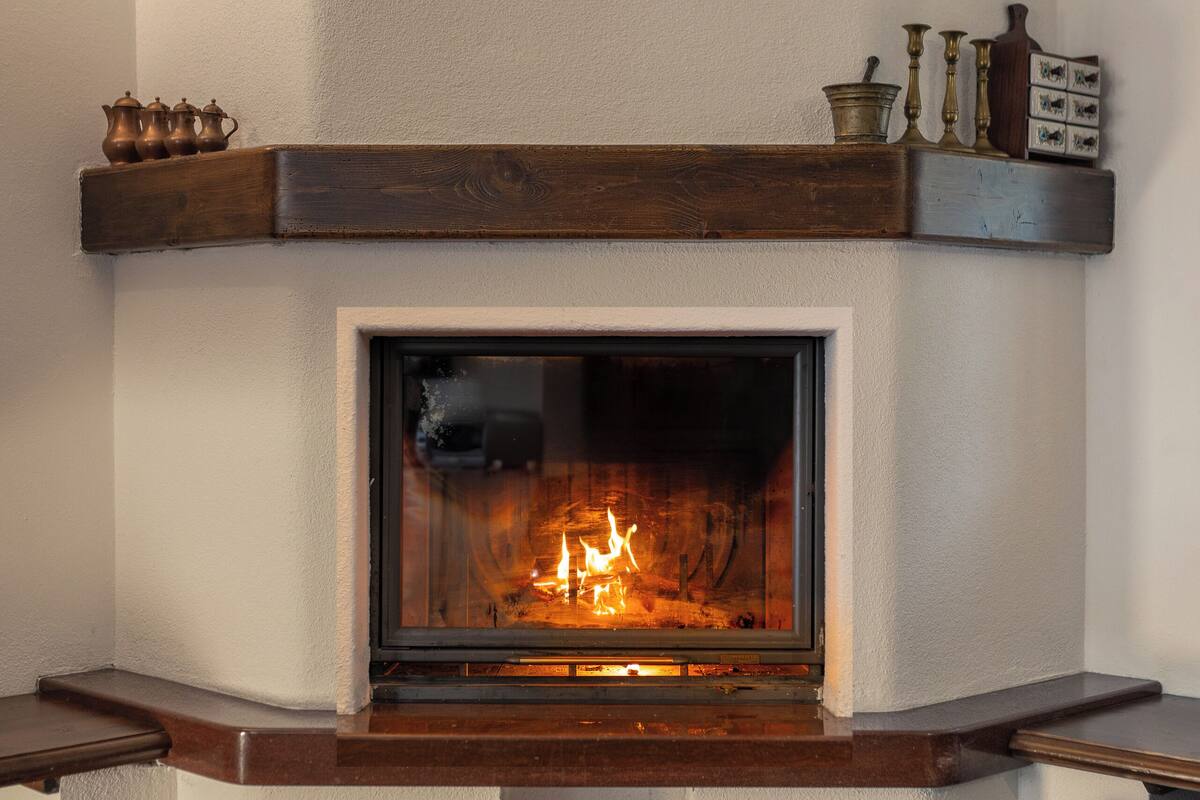 A fireplace with a fire, a wooden mantel, and a basket of firewood.