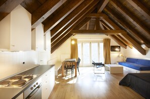 A modern kitchen with a central island, a dining area with a table and chairs, a sofa, and a large window with curtains. - Albergo Diffuso Comeglians (Comeglians)