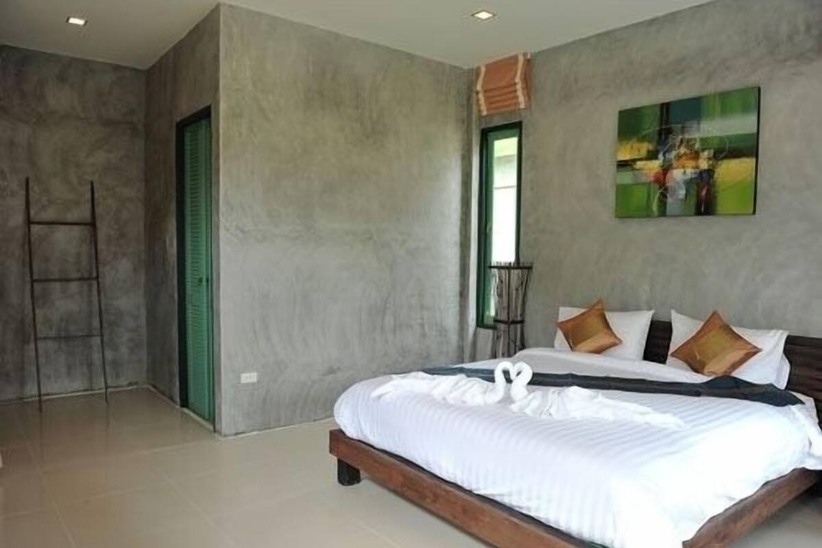 A modern bedroom with a large bed, a ladder, a window, and a painting on the wall.