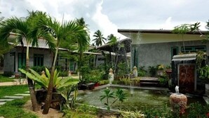 A garden with a pond, palm trees, and a house. - The Gleam Resort (Satun)