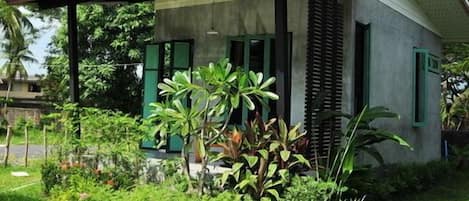 Una casa de un piso con techo inclinado, rodeada de exuberante vegetación y palmeras.