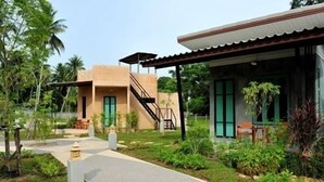 A two-story building with a covered porch, a staircase, and a garden area with plants and a small water feature. - The Gleam Resort (Satun)