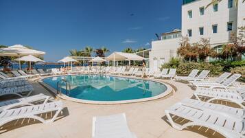 Una piscina al aire libre, sombrillas, sillones reclinables de piscina