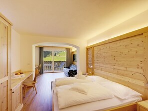 A bedroom with a wooden headboard, a bed with white linens, a desk with a chair, and a view of a balcony with outdoor furniture.