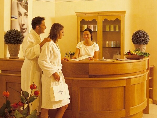 A reception area with a wooden reception desk, a receptionist, and two guests.