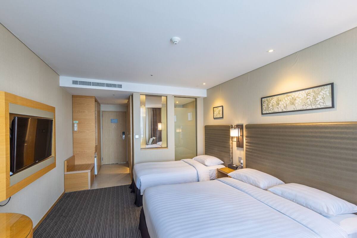 A hotel room with two beds, a TV, a desk, and a bathroom.
