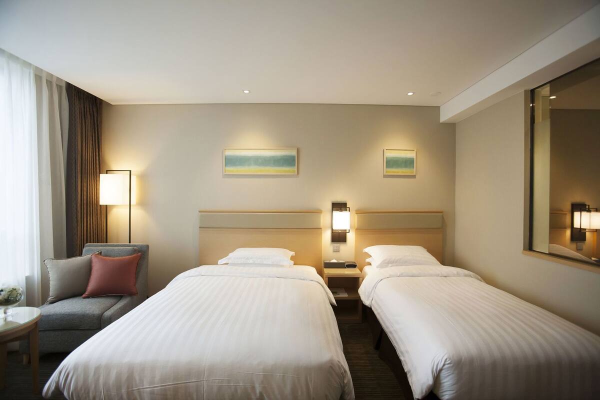 A hotel room with two single beds, a sofa, a nightstand, and a large mirror.