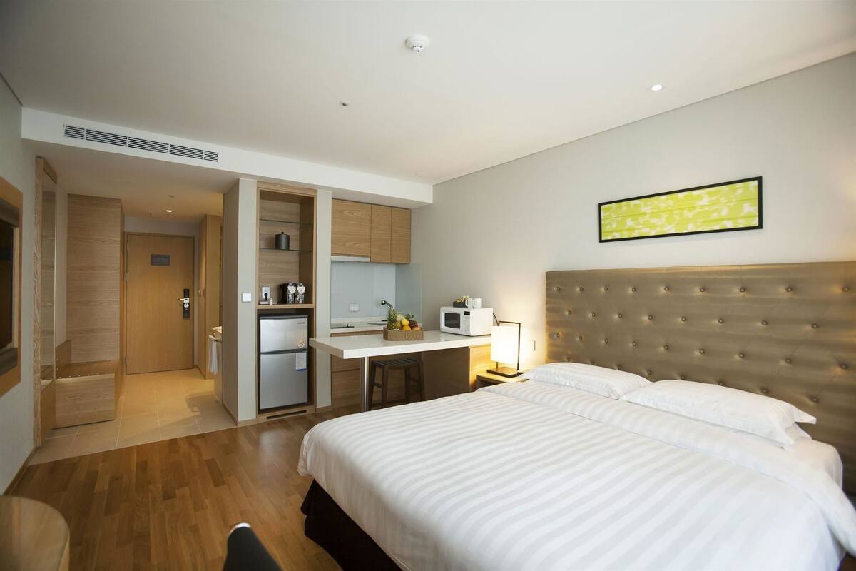 A hotel room with a bed, a desk, a microwave, and a kitchenette.