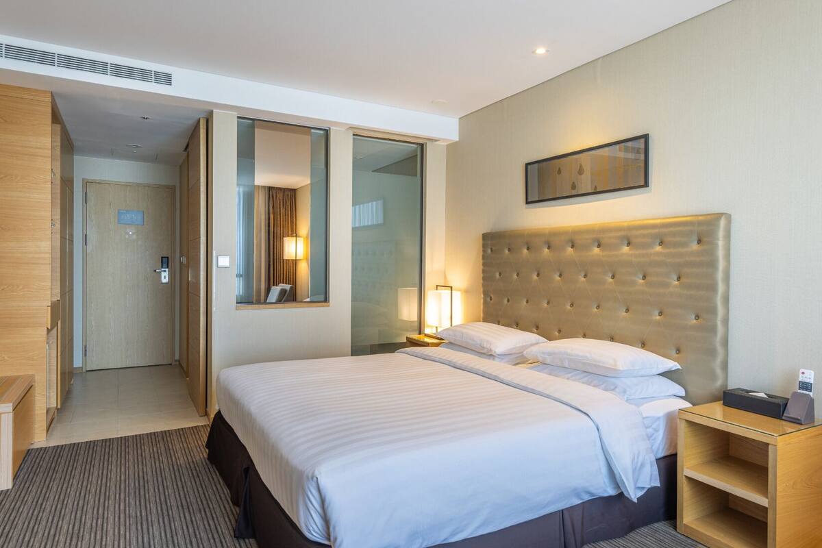 A hotel room with a large bed, a bedside table, a mirror, and a door leading to a bathroom.
