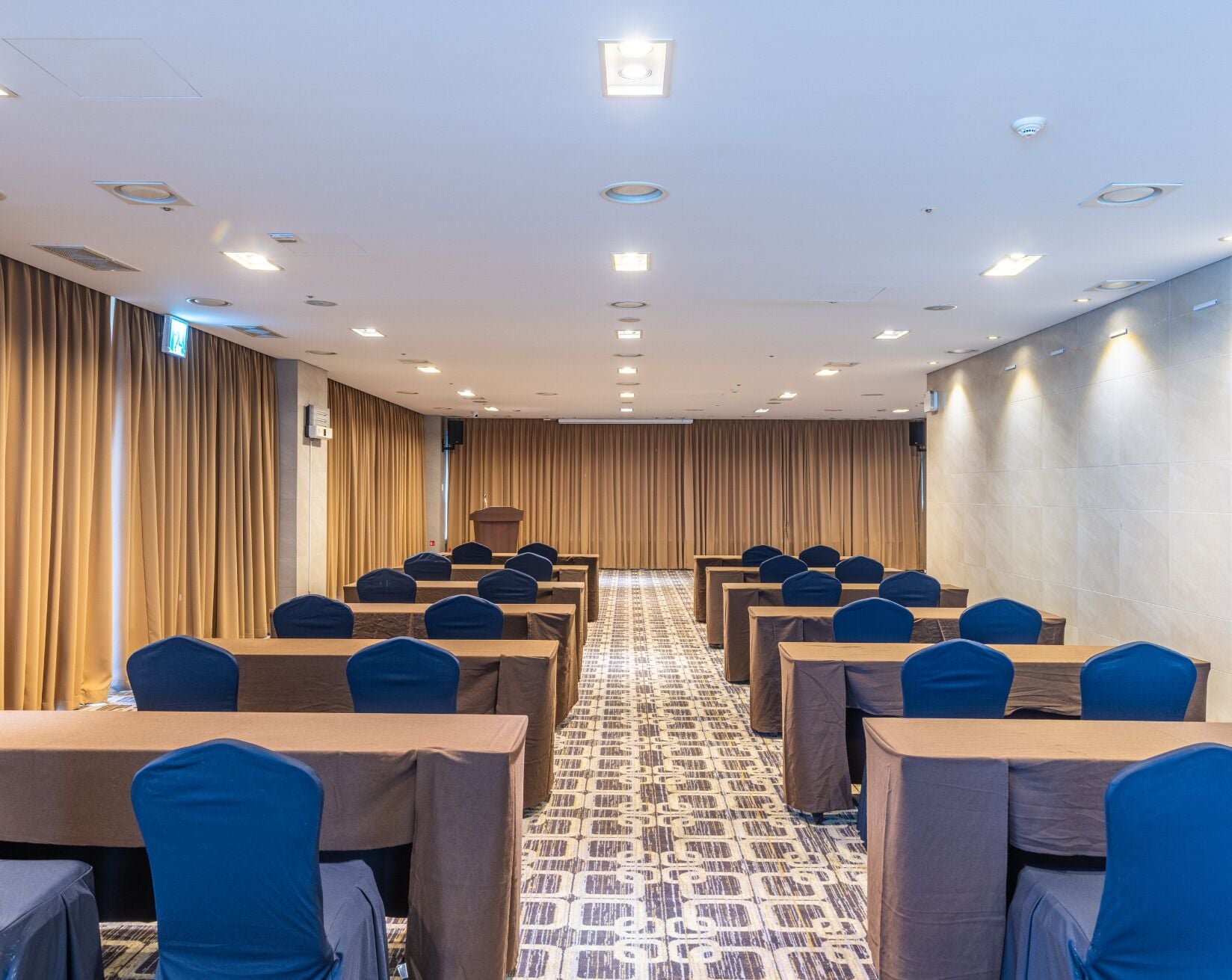 A conference room with rows of tables and chairs, a podium, and a patterned carpet.