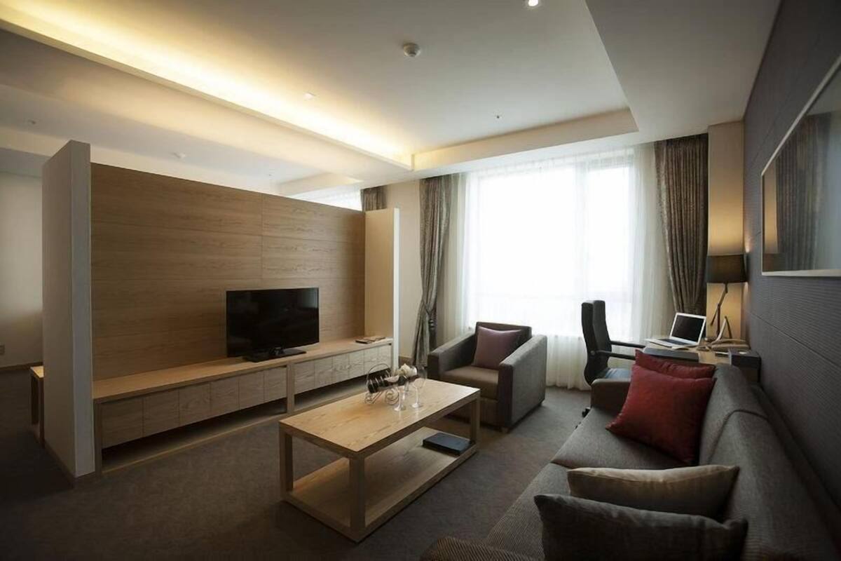 A modern hotel room with a flat-screen TV, a sofa, a coffee table, and a desk with a laptop.