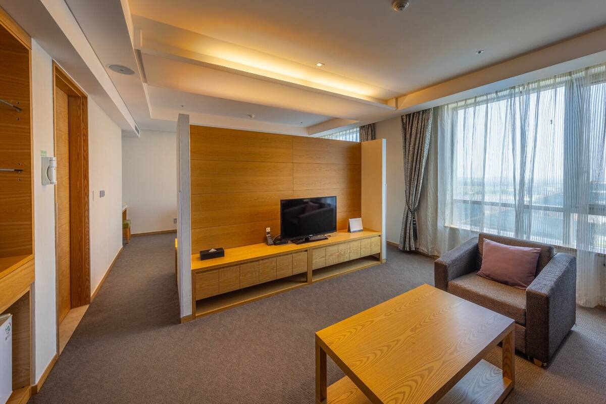A modern hotel room with a wooden entertainment unit, a flat-screen TV, a sofa, and a coffee table.