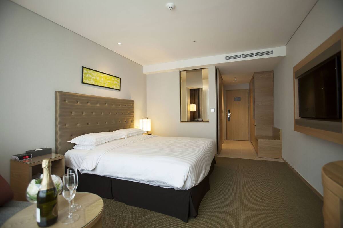A hotel room with a bed, bedside table, lamp, and a bottle of wine.