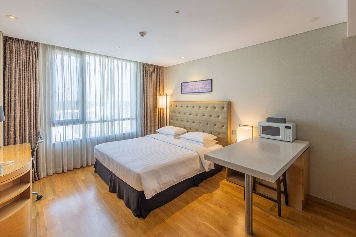 A hotel room with a bed, bedside table, lamp, and a microwave.