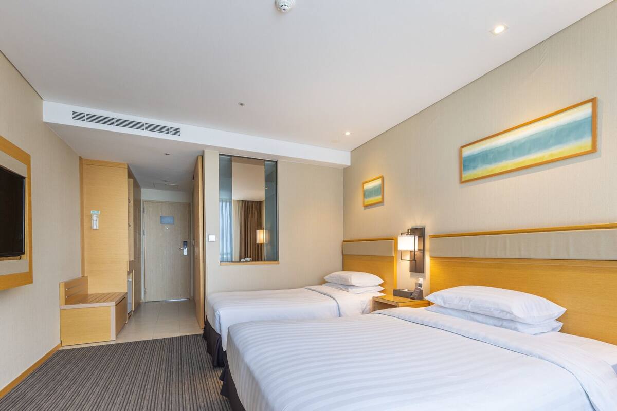 A hotel room with two beds, a large mirror, a painting, and a desk with a lamp.