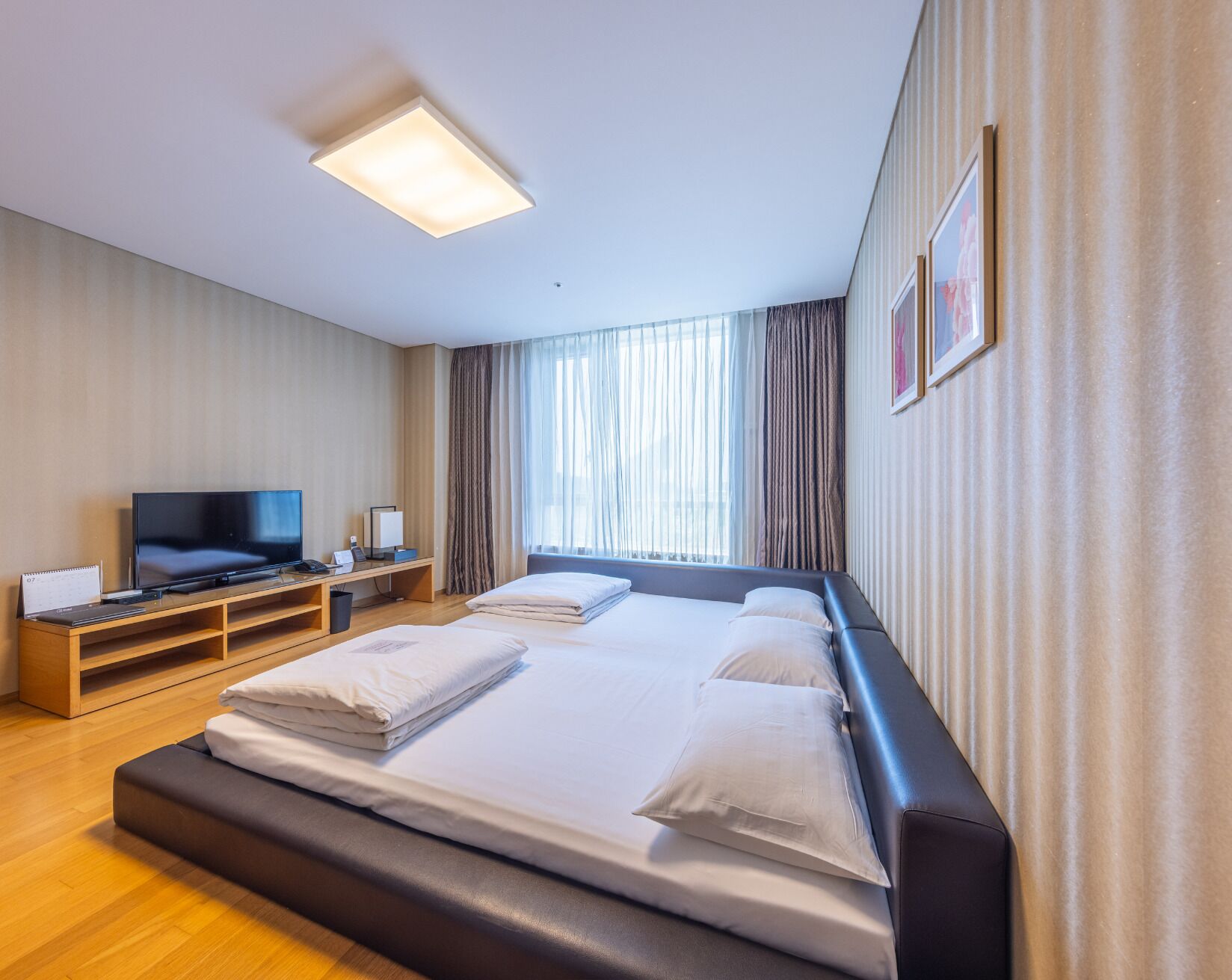 A hotel room with a large bed, a TV, a desk, and a window with curtains.