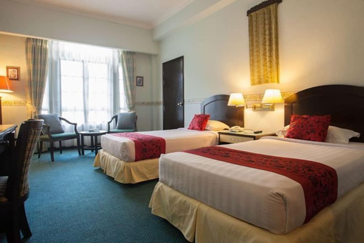 Une chambre d’hôtel avec deux lits, un bureau, une chaise et une fenêtre avec des rideaux.