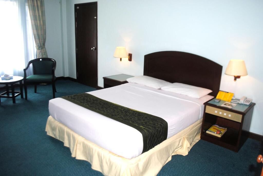 A hotel room with a large bed, two bedside tables, a chair, and a window with curtains.