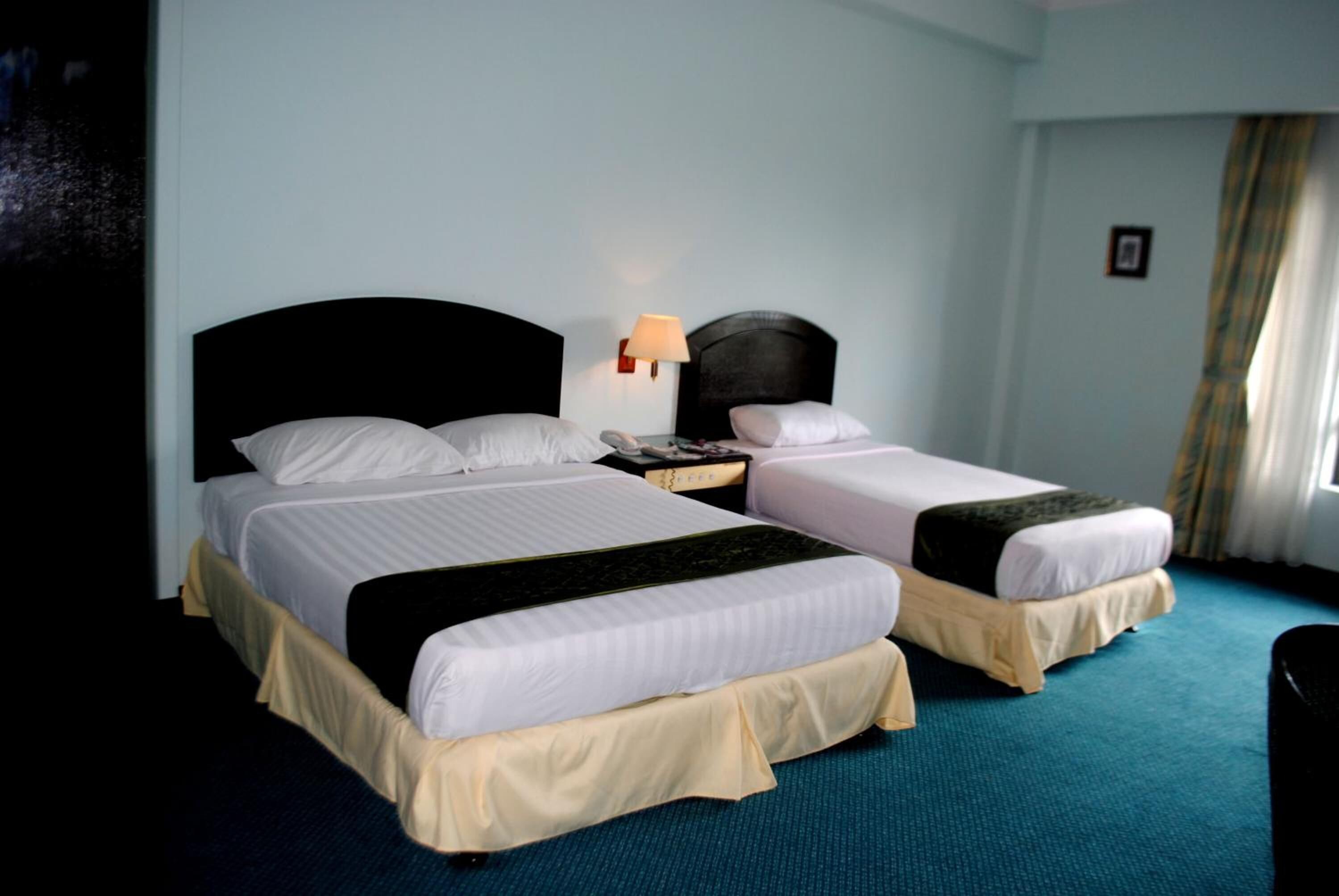 A hotel room with two beds, a nightstand, a lamp, and a window with curtains.